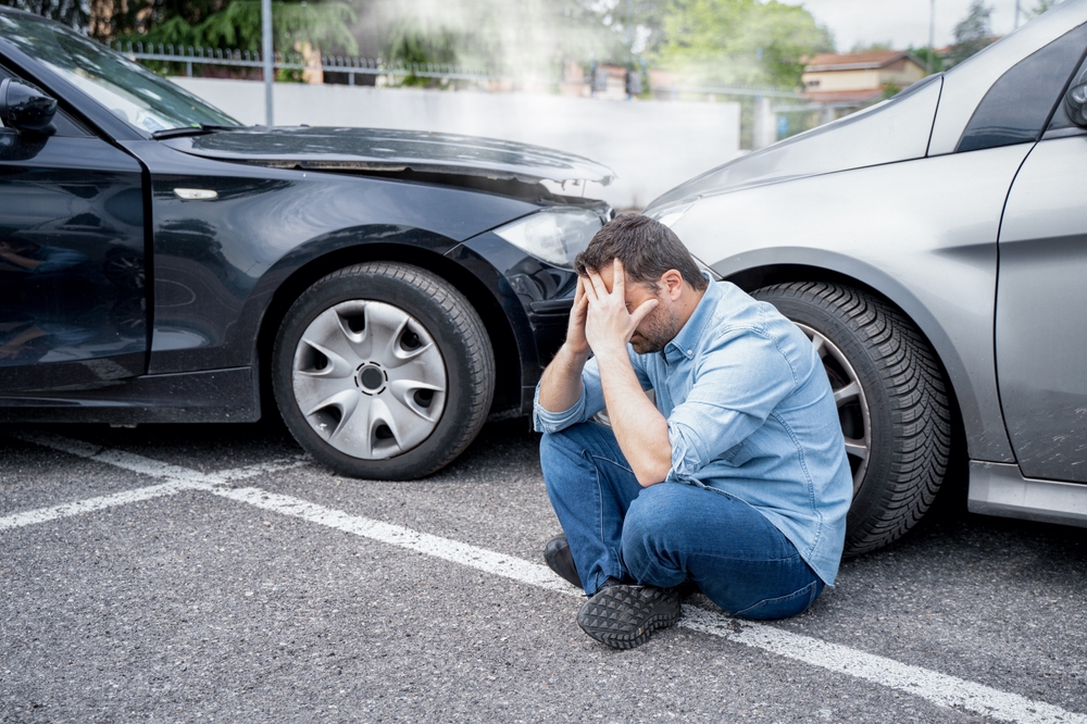 Man sitting on ground after two cars crashed