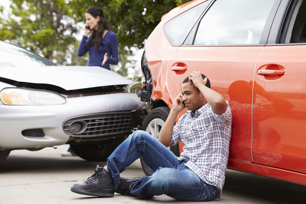 Male driver on cell phone after car accident in Florida with woman driver in background