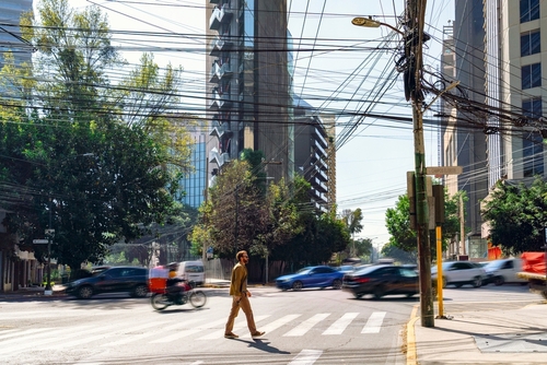 pedestrian crossing busy urban intersection with moving vehicles and overhead utility lines