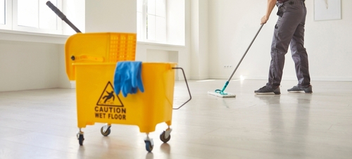 janitor mopping floor beside caution wet floor sign and mop bucket